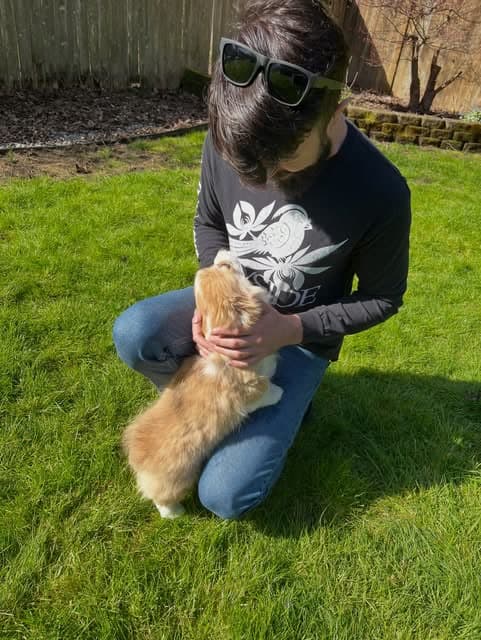 RJ crouched beside a small fluffy dog in a sunny yard.