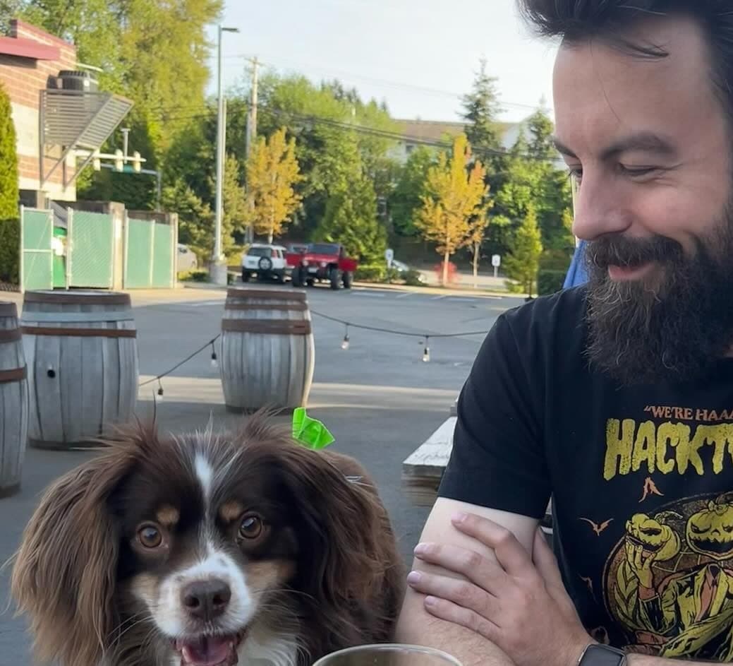 RJ smiling at Bear, their small brown-and-white long-haired dog, at an outdoor table.